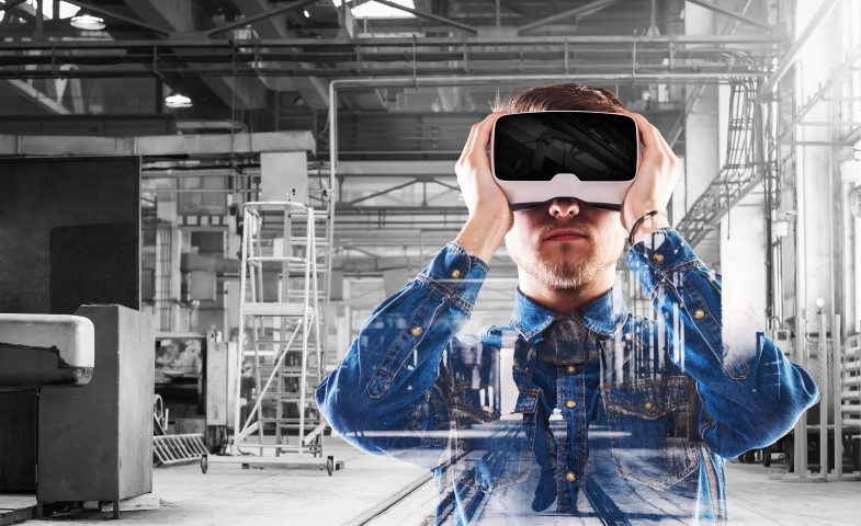 Hipster man in denim shirt wearing virtual reality goggles. Welding factory.