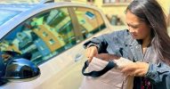 Eine Frau steht vor einem Auto und sucht etwas in ihrer Tasche.