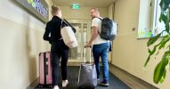 2 Personen mit Koffern und Rucksäcken verlassen ein Büro