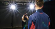 Eine Frau in einem Studio fotografiert einen Mann, der im Rampenlicht steht.