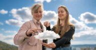 Zwei Frauen stehen vor einem Himmel mit Wolken und zeigen auf eine weitere Wolke in ihrer Hand.