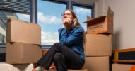 Frau sitzt vor Umzugskarton und überlegt, was sie einpacken soll.