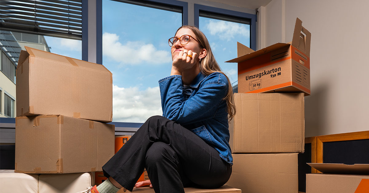 Frau sitzt vor Umzugskarton und überlegt, was sie einpacken soll.