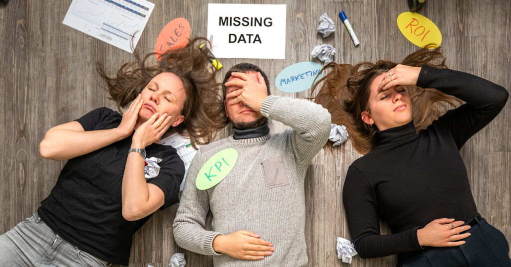 Drei Mitarbeiter liegt verzweifelt auf dem Boden. Sie sind umgeben von Papiermüll und ungenutzten Daten.