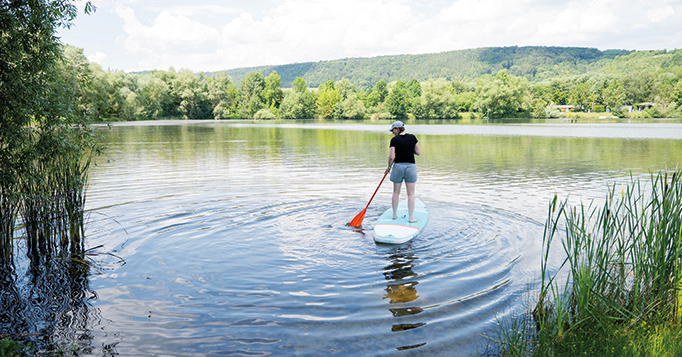 Frau auf einem Stand-up-Paddle hält Balance und steuert – Metapher für KI‑Ads mit Leitplanken.