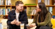 Zwei Personen sitzen sich in einem gemütlichen Raum mit Bücherregal gegenüber und unterhalten sich bei Getränken über User Research.