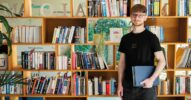 Junger Mann mit Abschlusskappe und Büchern vor einem Bücherregal als Symbol für Weiterbildung und Rollenwandel im KI-Zeitalter.