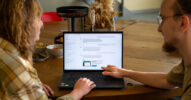 Zwei Personen betrachten gemeinsam eine ChatGPT-Unterhaltung auf einem Laptop. Unterhalb der Antwort ist eine als gesponsert gekennzeichnete Anzeige eingeblendet.