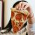 Frau hält ein Stück Pizza in die Kamera.