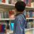 Kleines Kind steht in einer Bibliothek vor dem Bücherregal